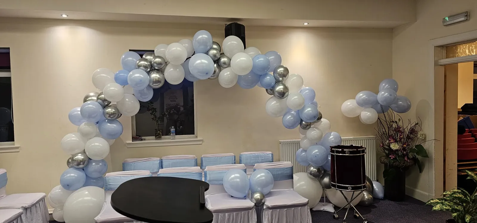 Pale blue and white balloon arch with silver accents over seating