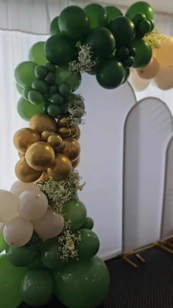 Green, gold and ivory balloons beside two white event backdrops