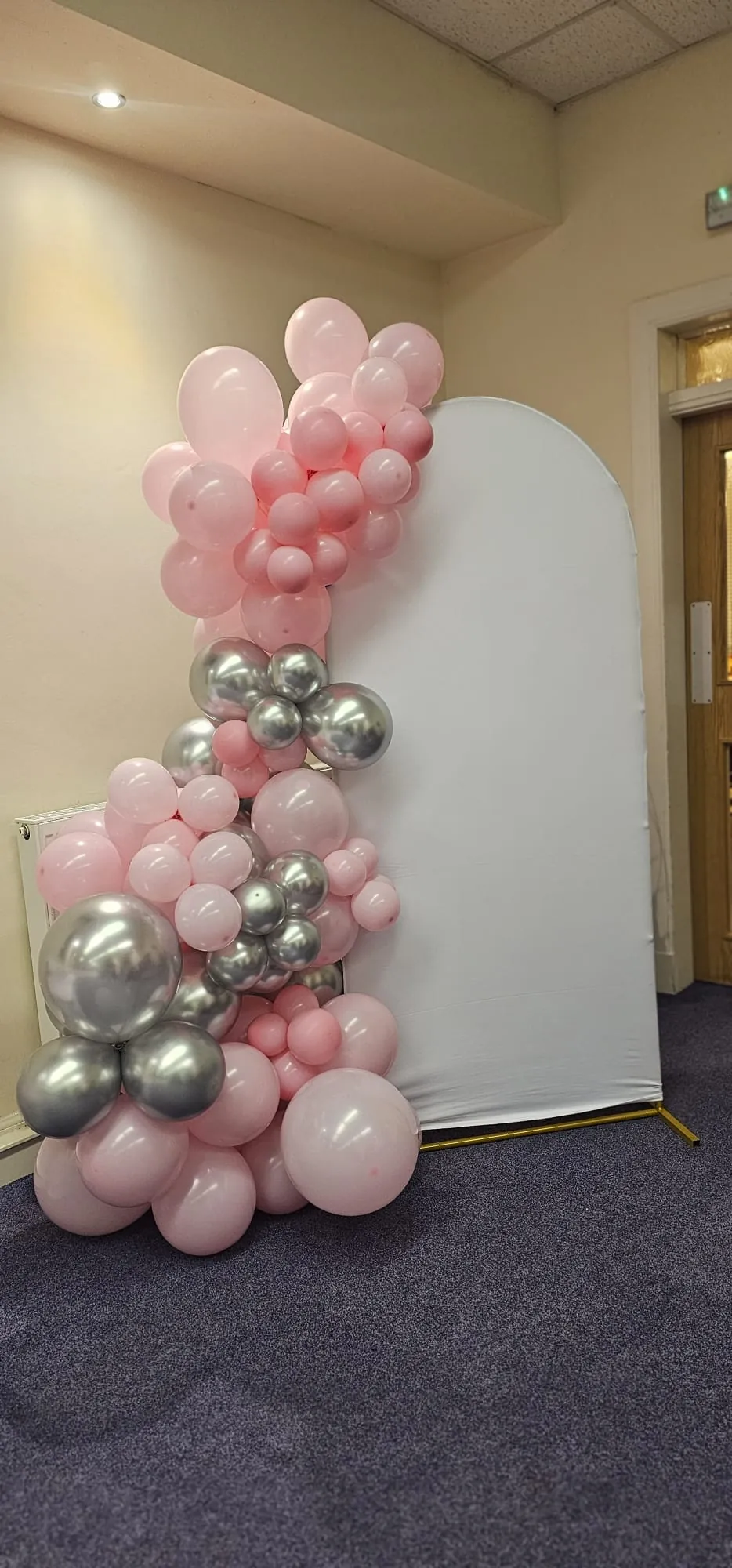 Pastel pink balloons with silver accents beside a white event backdrop